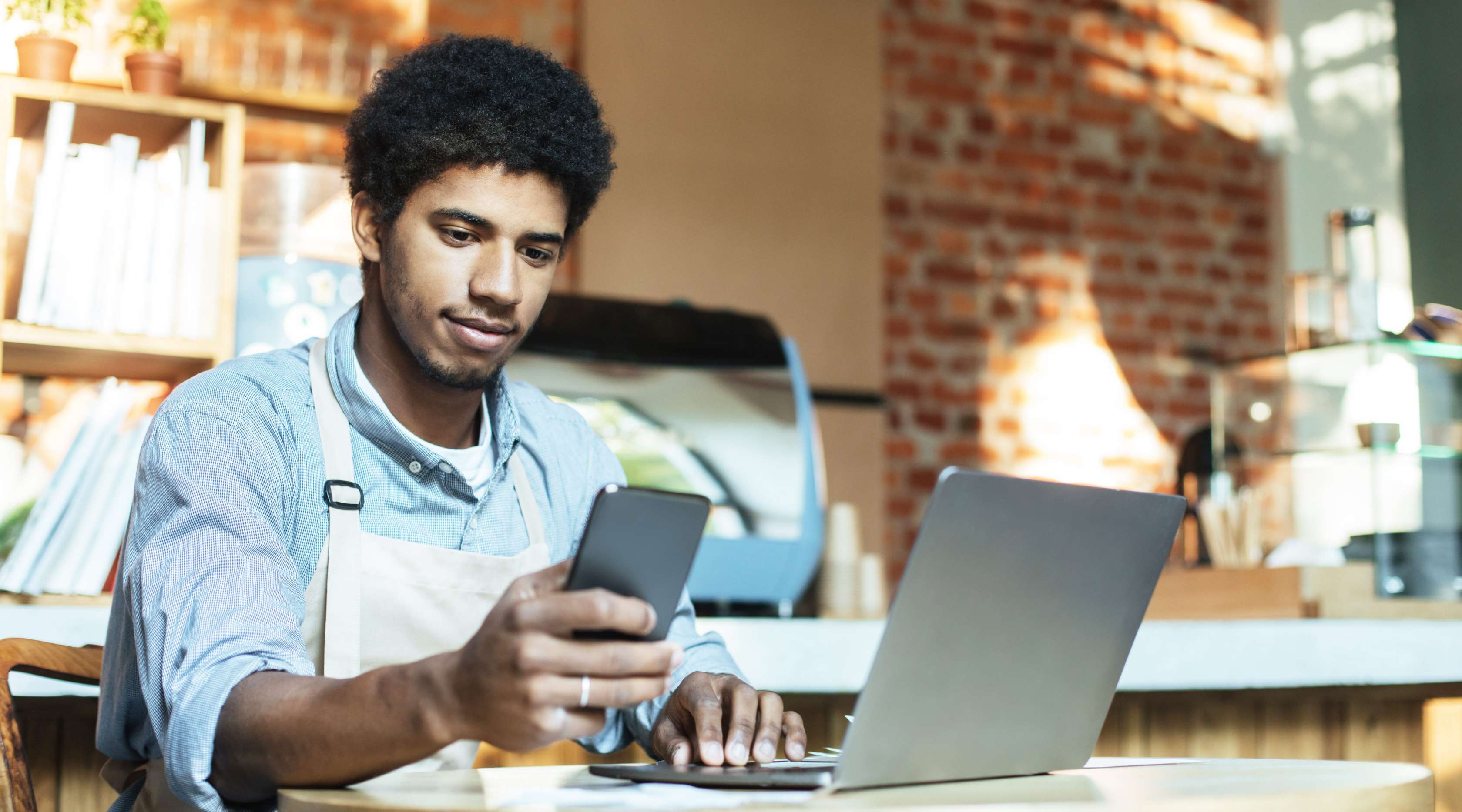 Junger Cafe-Angestellter sitzt im Cafe an einem Laptop