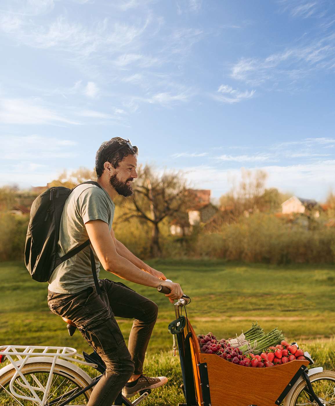 Mann fährt mit einem Lastenrad mit Gemüse beladen über einen Feldweg