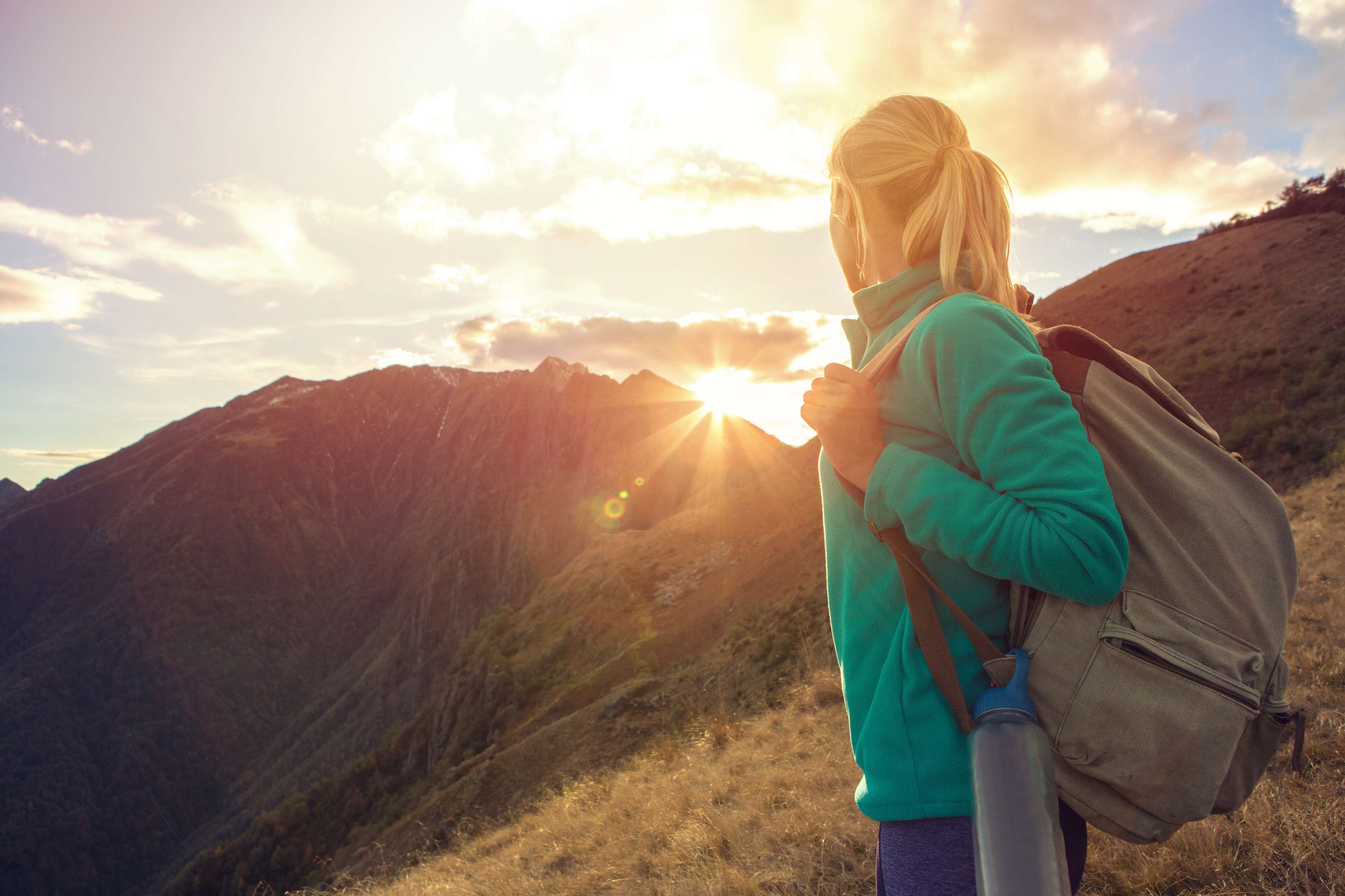 Allianz - Krankenversicherung Urlaub: Junge Frau wandert in den Bergen bei Sonnenuntergang