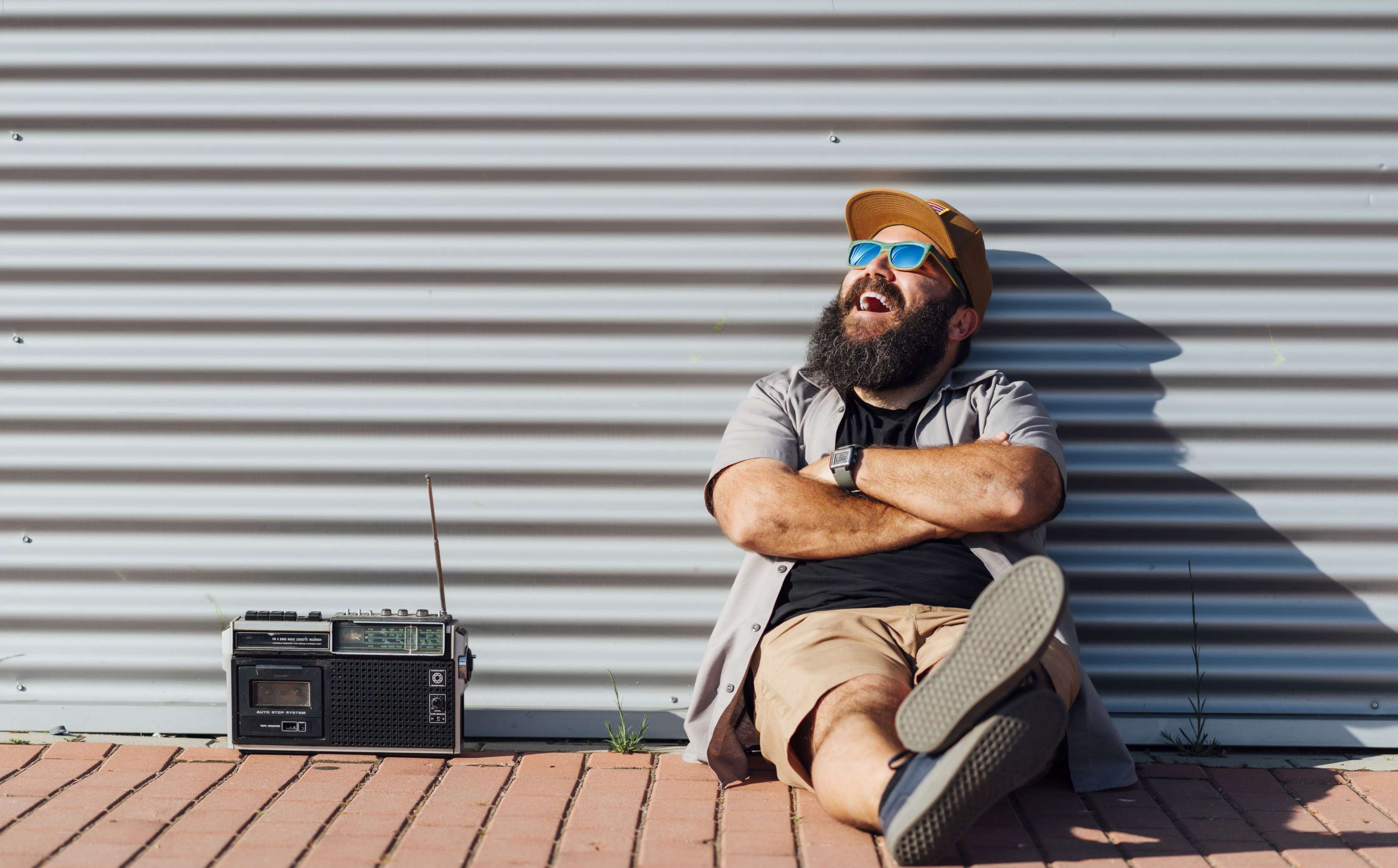 Ein Mann lehnt lachend an einer Wand, neben ihm steht ein Radio
