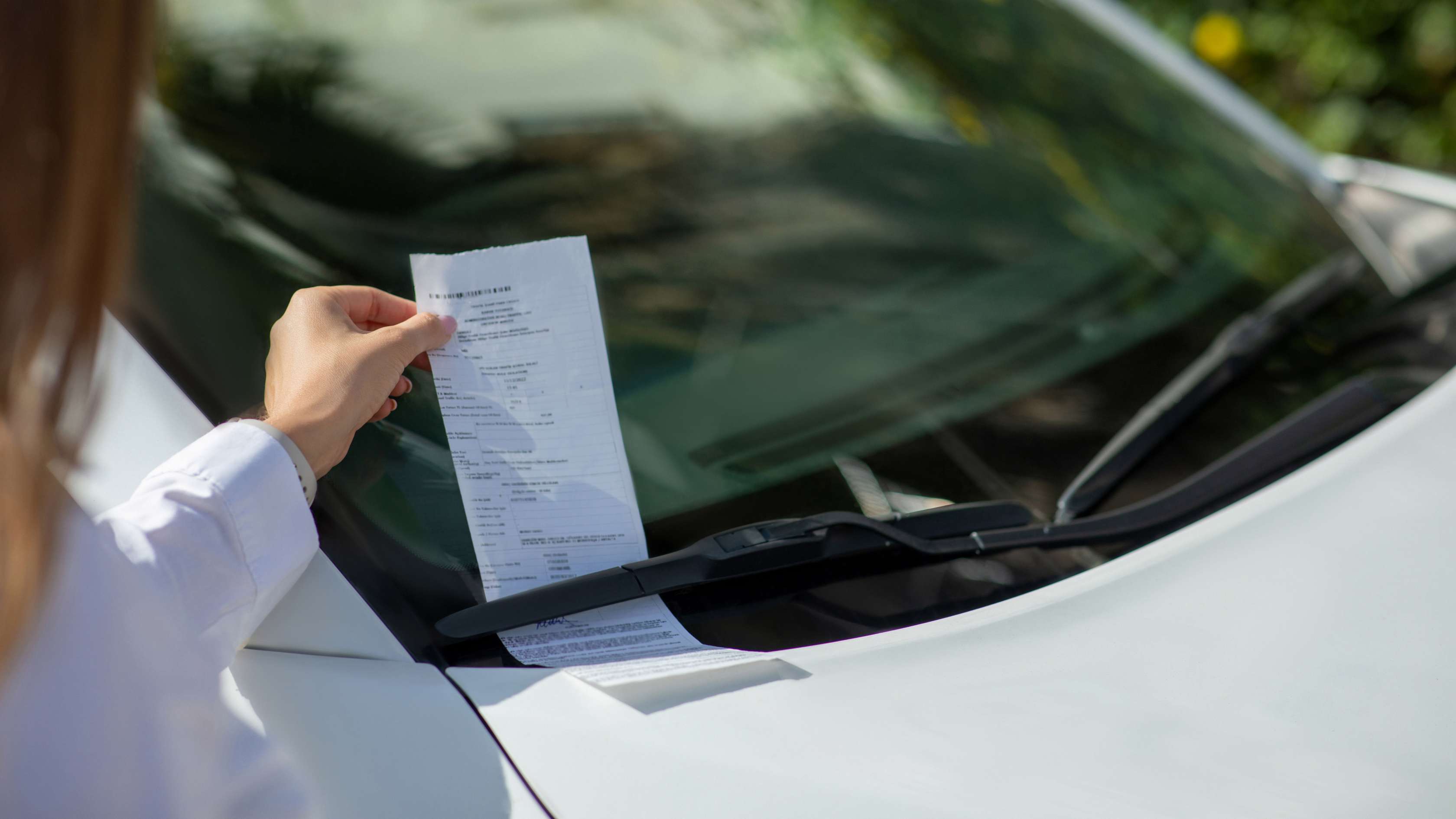 Frau nimmt Strafzettel von der Windschutzscheibe ihres Autos