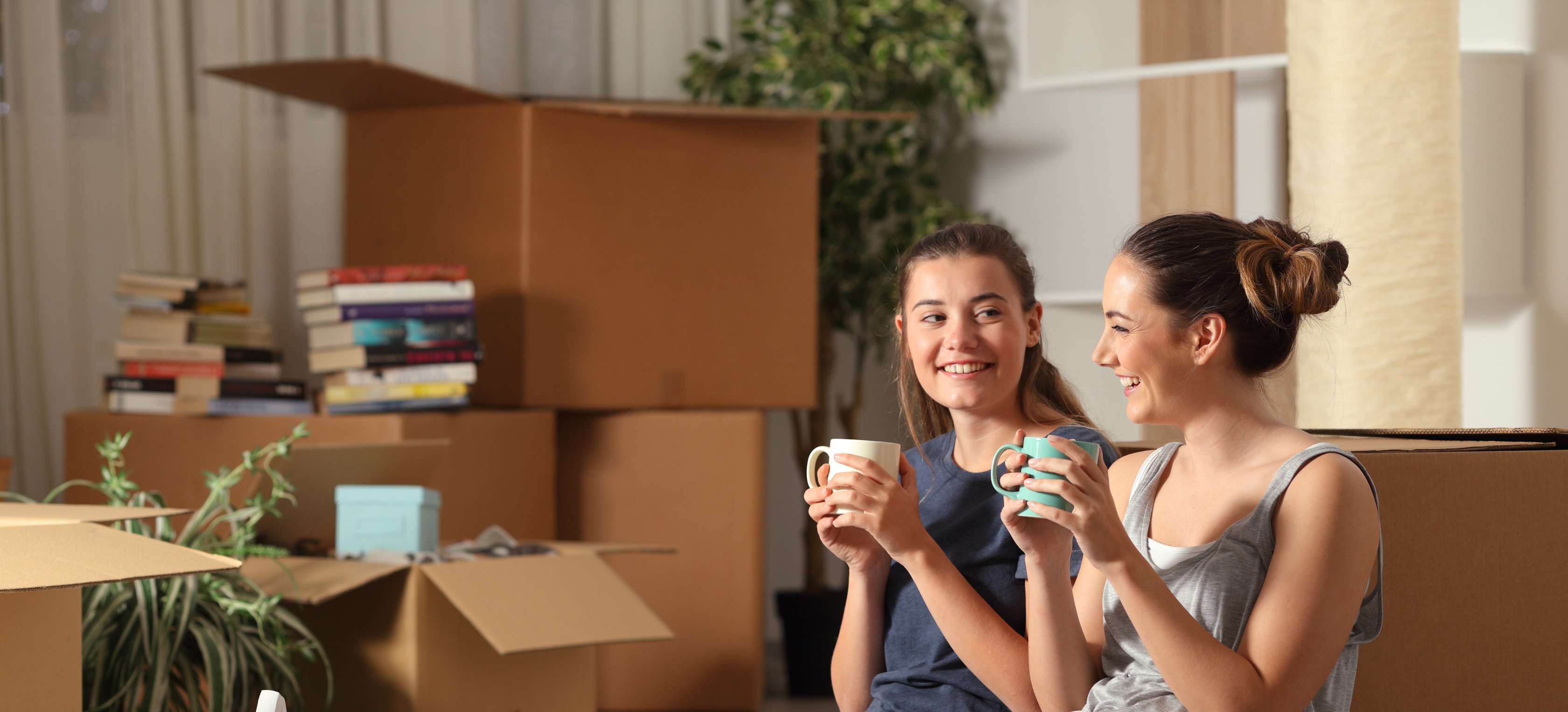 Zwei Mädchen sitzen vor Umzugskartons und trinken Kaffee