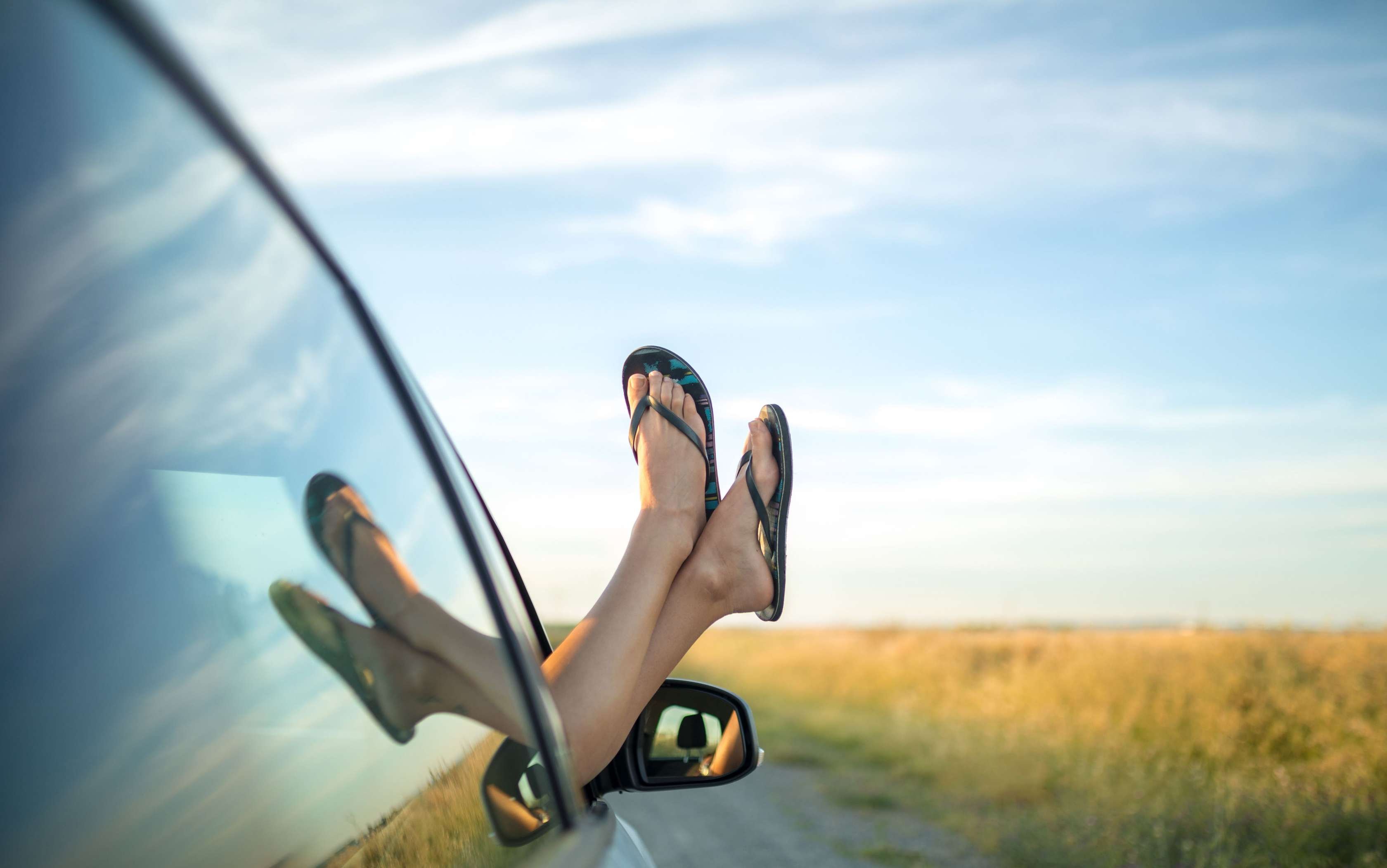 Ein Paar Füße mit Flipflops werden aus einem Autofenster herausgestreckt