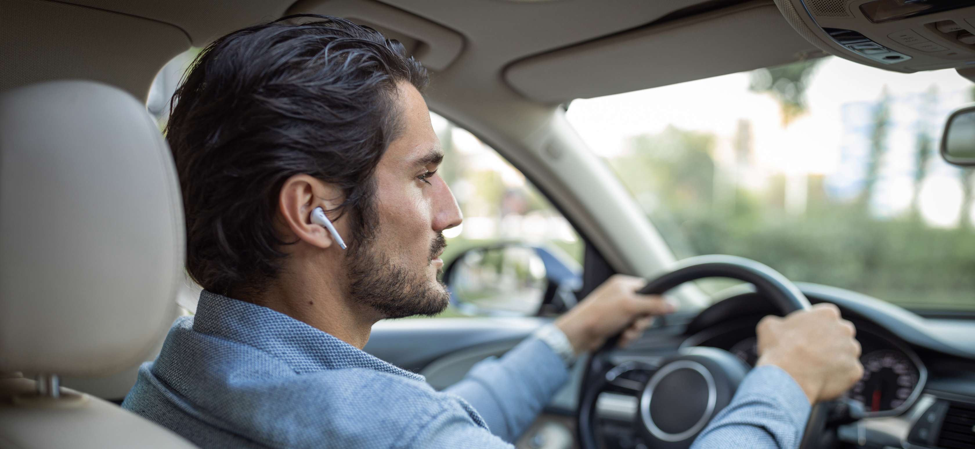 Ein Mann fährt Auto, während er kabellose Kopfhörer in den Ohren trägt