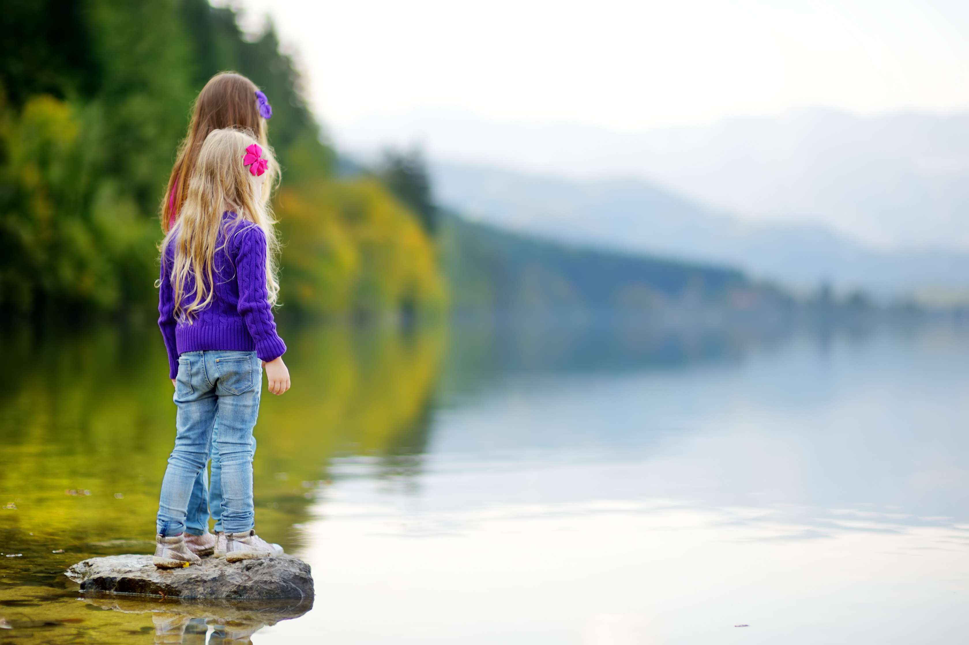 Zwei Mädchen stehen auf einem Stein und blicken auf den Hallstadter See.