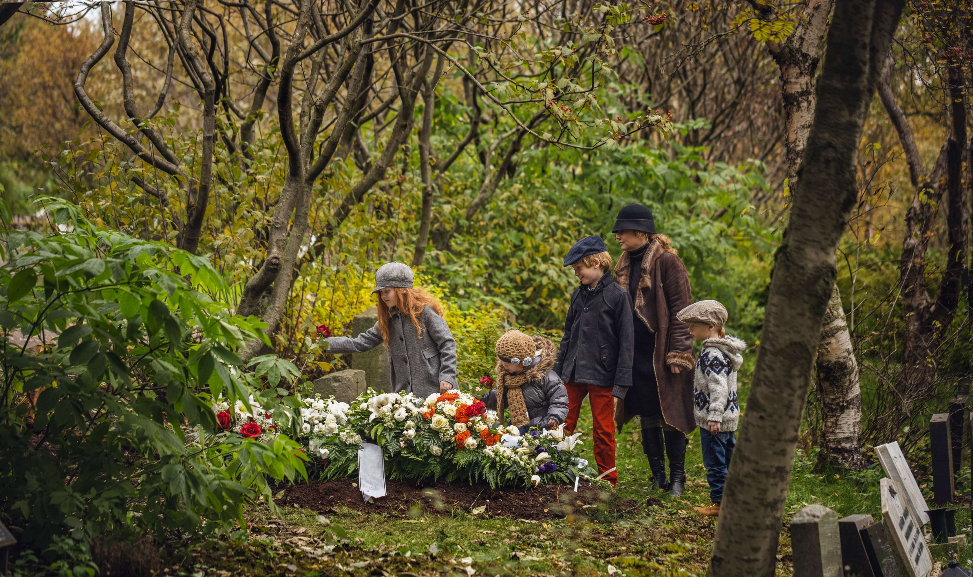 Feuerbestattung - eine Mutter mit vier Kindern steht an einem Grab mit Blumenschmuck